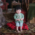Load image into Gallery viewer, Child-sized doll in a green outfit sitting on a red cushion with a vintage room background.