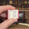 Load image into Gallery viewer, Hand holding a small book titled 'Plain Jane Vanilla' with a blurred bookshelf background.