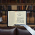 Load image into Gallery viewer, Open book titled 'The Gospel According to Mark' held open by a pair of tweezers with a blurred bookshelf background.