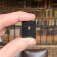 Load image into Gallery viewer, Hand holding a small black book with a gold cross in front of a blurred bookshelf.