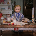 Load image into Gallery viewer, Doll in a checkered outfit sitting at a table with various holiday items in a room setting.