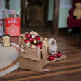 Load image into Gallery viewer, Small cat with Christmas ornaments in a cardboard box on a wooden floor.