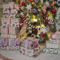 Load image into Gallery viewer, Stacks of Christmas presents with a decorated tree in the background
