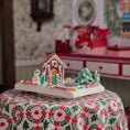 Load image into Gallery viewer, Gingerbread house with candy decorations on a floral tablecloth