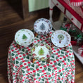 Load image into Gallery viewer, Four decorative plates with Christmas tree designs on a tablecloth with holly pattern.