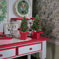 Load image into Gallery viewer, Two small Christmas trees with red ribbons on a red and white cabinet.