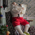 Load image into Gallery viewer, Santa Claus sitting in a chair reading a letter in a cozy room with floral wallpaper.