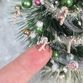 Load image into Gallery viewer, Close-up of a decorated Christmas tree branch with candy canes and ornaments, held by a hand.