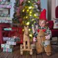 Load image into Gallery viewer, Clay elf character with a wooden horse in a festive setting with Christmas tree and presents.