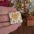 Load image into Gallery viewer, Miniature gift box with a gold bow held in a hand, with a festive background.