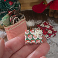 Load image into Gallery viewer, Miniature Christmas gift box with Santa Claus pattern held in a hand, with a decorated tree and stockings in the background.