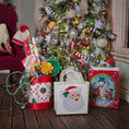 Load image into Gallery viewer, Decorative Christmas items including a gift bag with a Santa Claus design in front of a decorated tree.