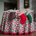 Load image into Gallery viewer, holiday tablecloth with floral pattern and decorative stockings on wooden clothing pins.