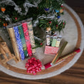 Load image into Gallery viewer, Decorative rolls of paper and bow on a round rug with a Christmas tree in the background.