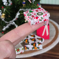Load image into Gallery viewer, Hand holding a small Miniature dollhouse box with Christmas patterns in front of a decorated Christmas tree.