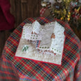 Load image into Gallery viewer, Decorative gingerbread house on a plaid surface with a blurred background, top view