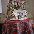 Load image into Gallery viewer, Gingerbread house on a plaid tablecloth with a decorated Christmas tree in the background