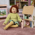 Load image into Gallery viewer, Catherine Muniere doll wearing a sweater sitting on the floor with a dollhouse and toys in the background.