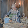 Load image into Gallery viewer, Vintage-style doll in a decorative setting with a table and ornate background