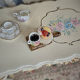 Load image into Gallery viewer, Tea cup and cupcake on a decorative table.