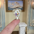 Load image into Gallery viewer, Miniature ornate vase held on a single finger with a decorative interior background