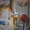 Load image into Gallery viewer, Decorative figurine on a gold pedestal in an ornate room with a chair and floral arrangement.