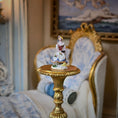 Load image into Gallery viewer, Decorative figurine on a gold pedestal in an elegant room with a chair and painting in the background.