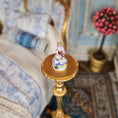 Load image into Gallery viewer, Decorative element with a small figurine on a gold base against a blurred background