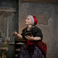 Load image into Gallery viewer, A detailed miniature elderly woman doll with gray hair, wearing a red headscarf, black top, and a purple patterned skirt, holding tarot cards in a dimly lit room.