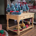 Load image into Gallery viewer, Decorative Christmas trees and presents on a wooden table with a festive background.