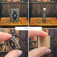 Load image into Gallery viewer, Collage of a miniature book with a dark cover and gold detailing, held open to reveal text, on a wooden surface with a bookshelf background.