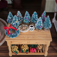 Load image into Gallery viewer, Decorative Christmas scene with miniature trees, wreath, and cookies on a wooden table.