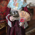Load image into Gallery viewer, Close up of Geisha doll wearing a traditional outfit with a decorative fan in a warm-toned interior setting