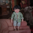 Load image into Gallery viewer, Miniature Chinese dollhouse character doll by Svetlana Blasing with a green patterned shirt held in a hand, with a blurred background