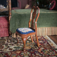 Load image into Gallery viewer, Wooden chair with a scenic petit point cushion on a rug in a room with green bed and red accents
