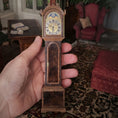 Load image into Gallery viewer, Hand holding a miniature wooden clock with intricate design in a room setting.