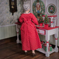 Load image into Gallery viewer, Woman in a red dress with white polka dots standing in a room decorated for Christmas.
