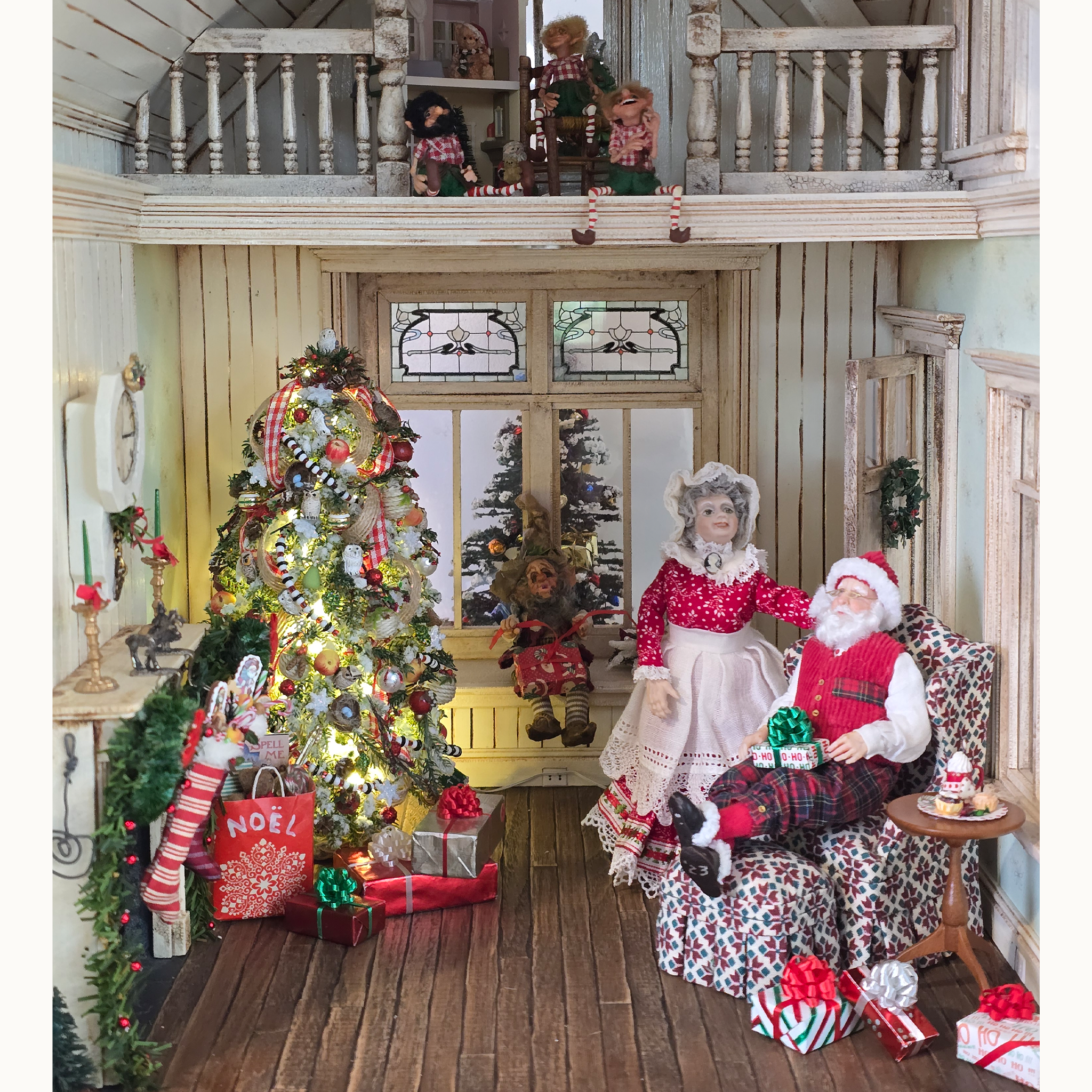 Decorative indoor scene with a Christmas tree, dolls, and festive decorations in a miniature house.