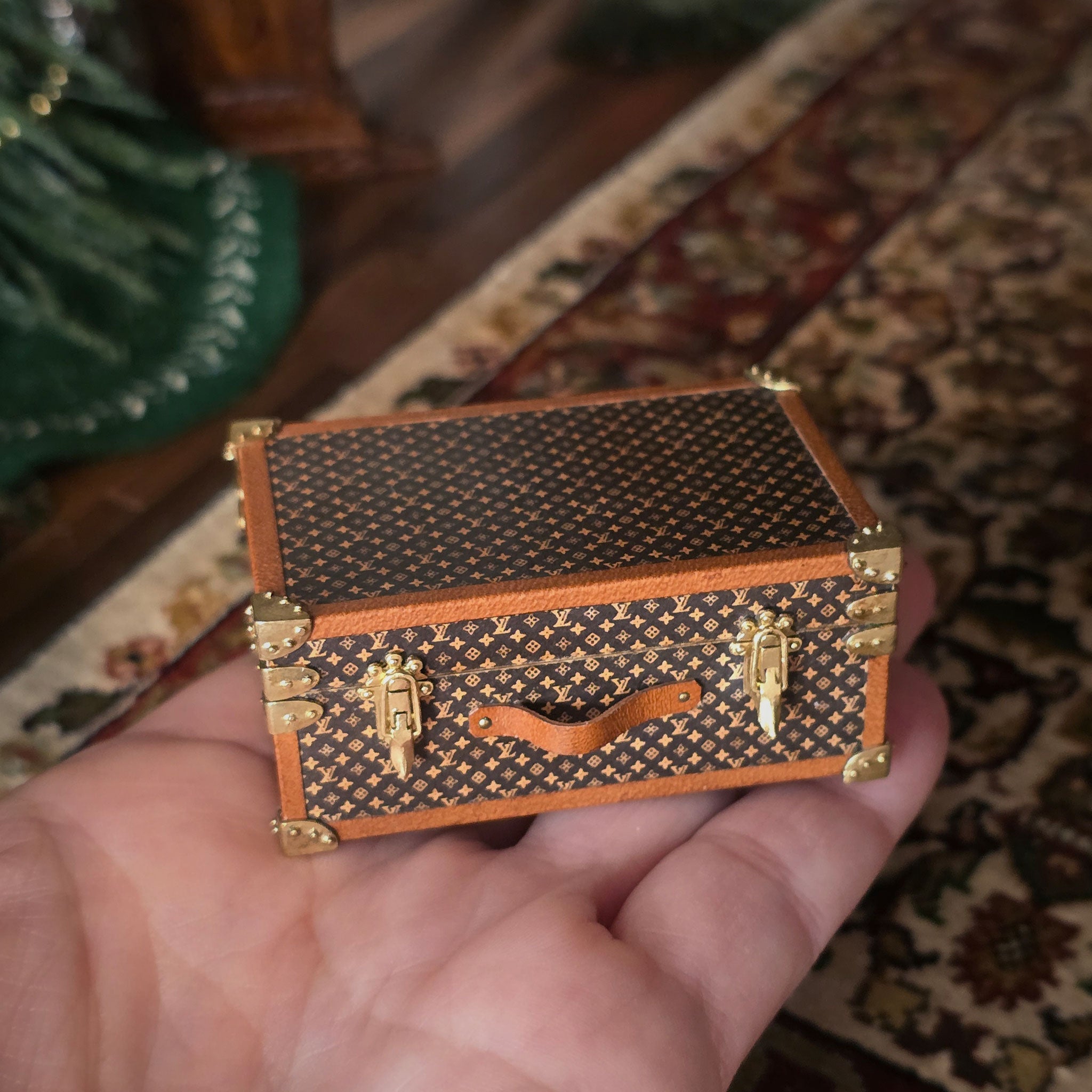 Miniature patterned suitcase held in a hand on a textured surface