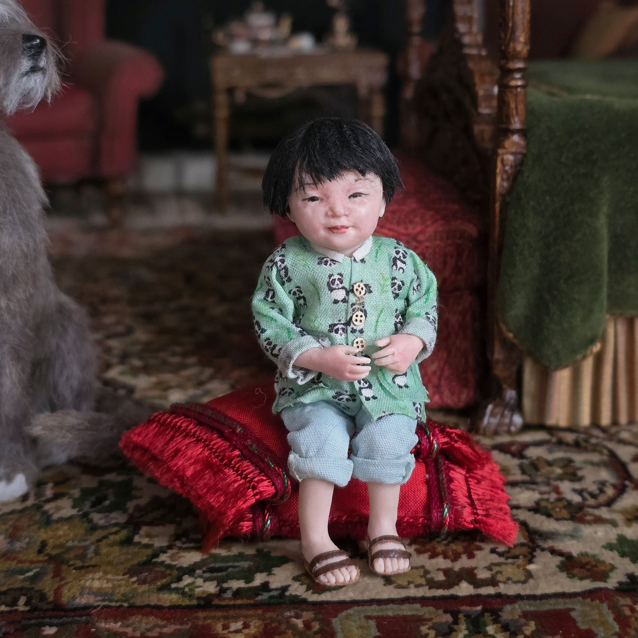 Child-sized doll in a green outfit sitting on a red cushion with a vintage room background.