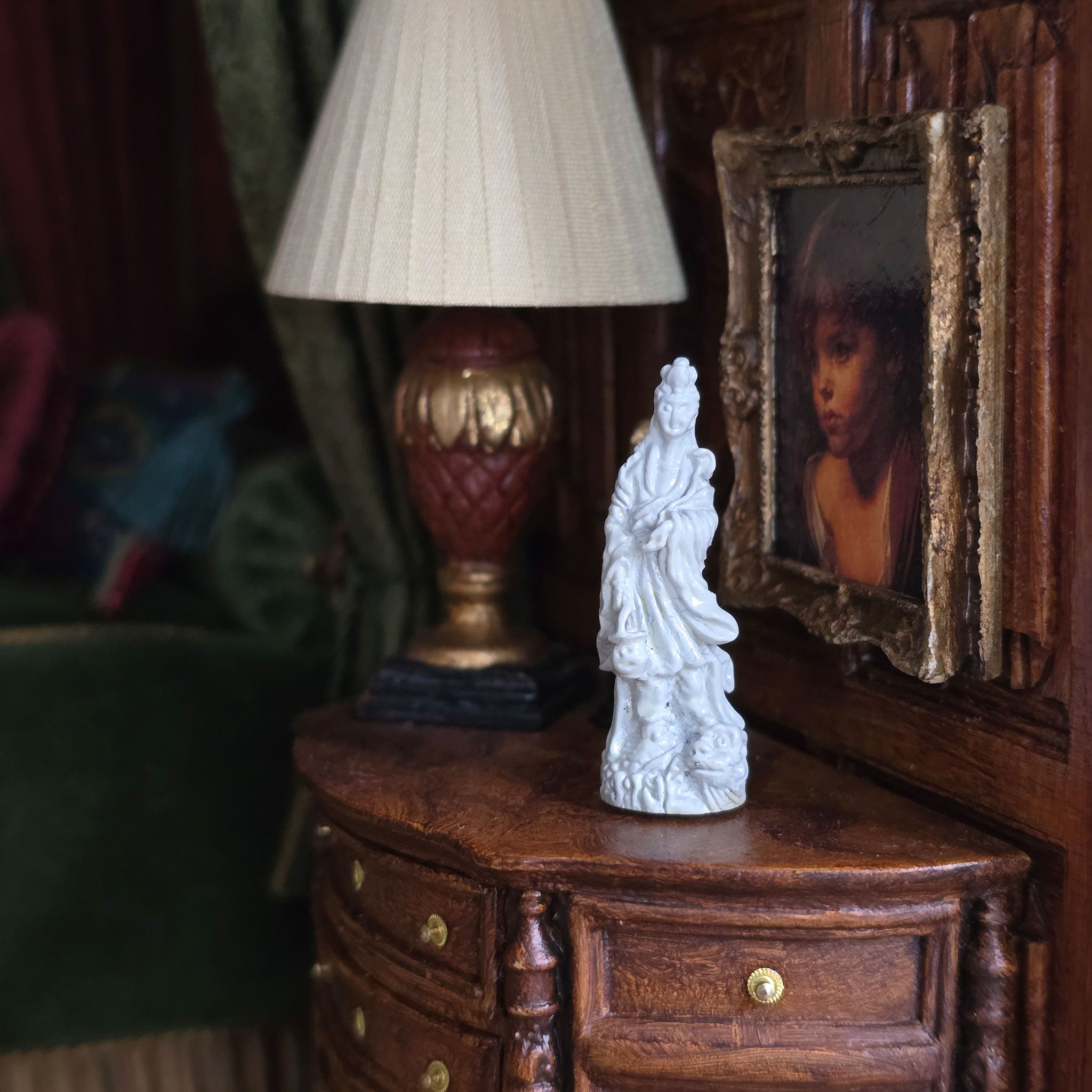 Vintage-style interior with a lamp, statue, and framed portrait on a wooden surface.