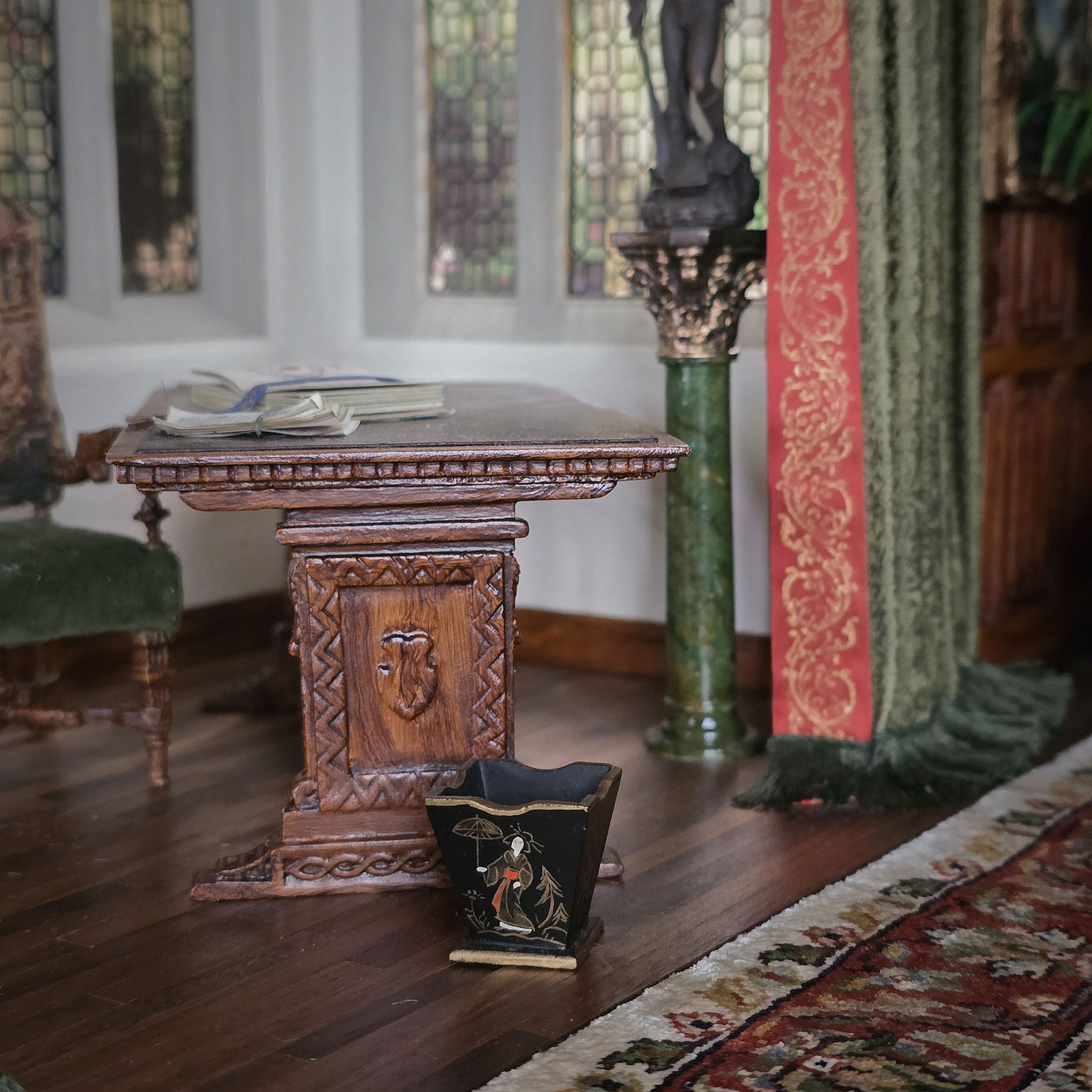 Carved wooden table in a room with stained glass windows and decorative elements, including a painted wastebasket.