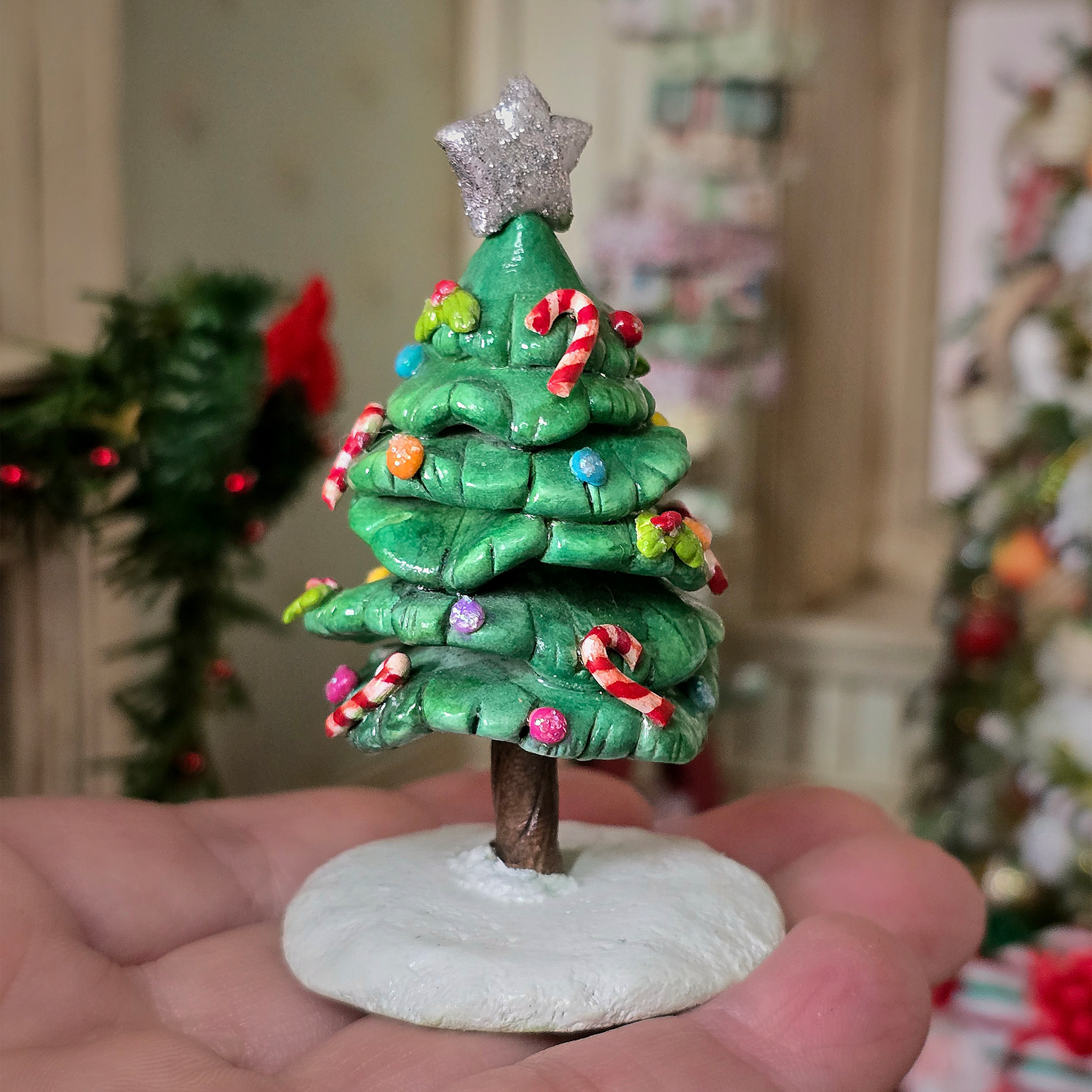 Small green Christmas tree figurine with decorations held in a hand against a festive background.