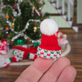 Load image into Gallery viewer, Miniature knitted hat with a white pom-pom held in front of a decorated Christmas tree.
