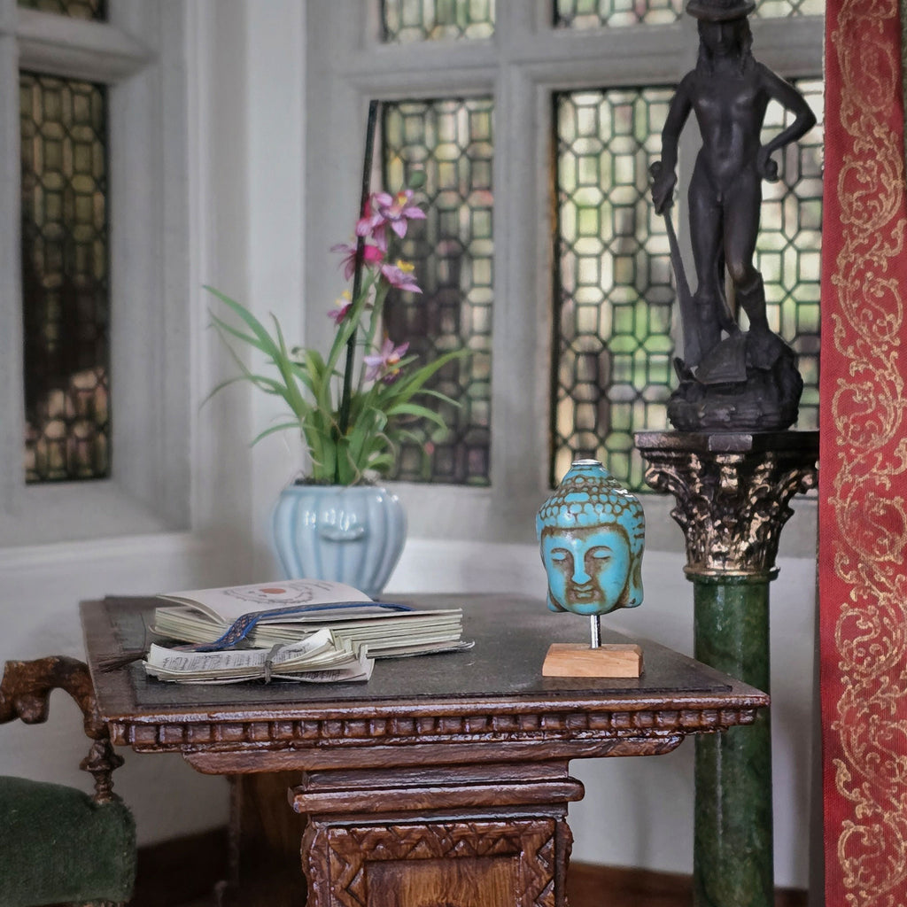 Decorative table with books, a vase, and a statue in a room with stained glass windows.