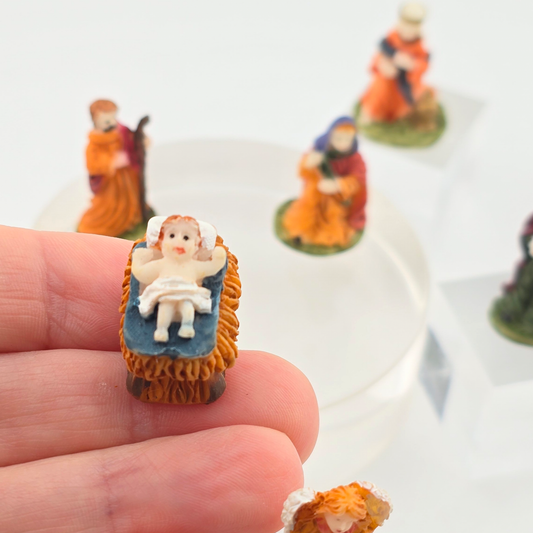 dollhouse Miniature baby Jesus in the Manger figurine, held between fingers with other similar figurines in the background