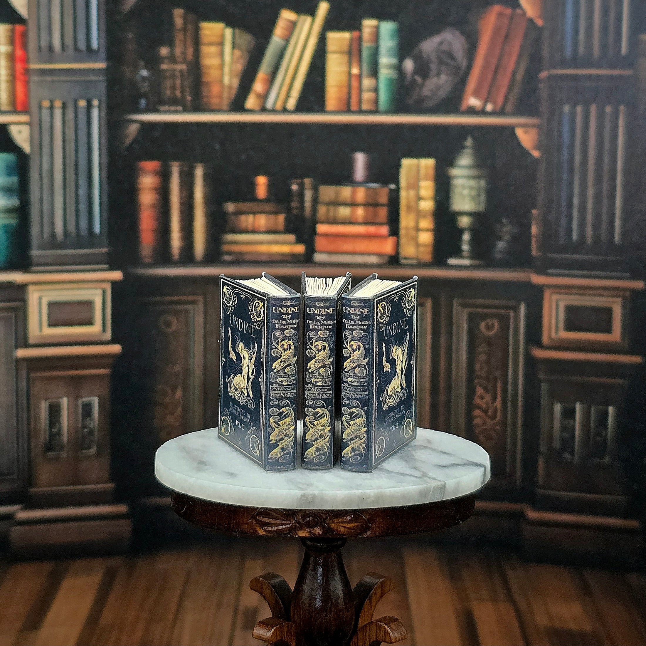 Three ornate books on a marble surface with a bookshelf background