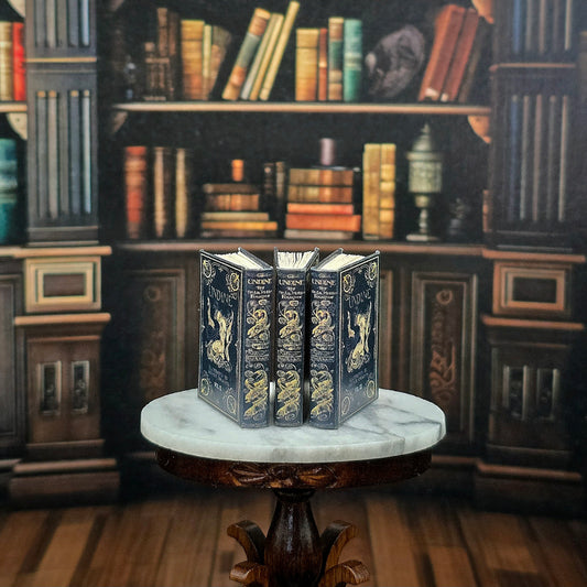 Three ornate books on a marble surface with a bookshelf background