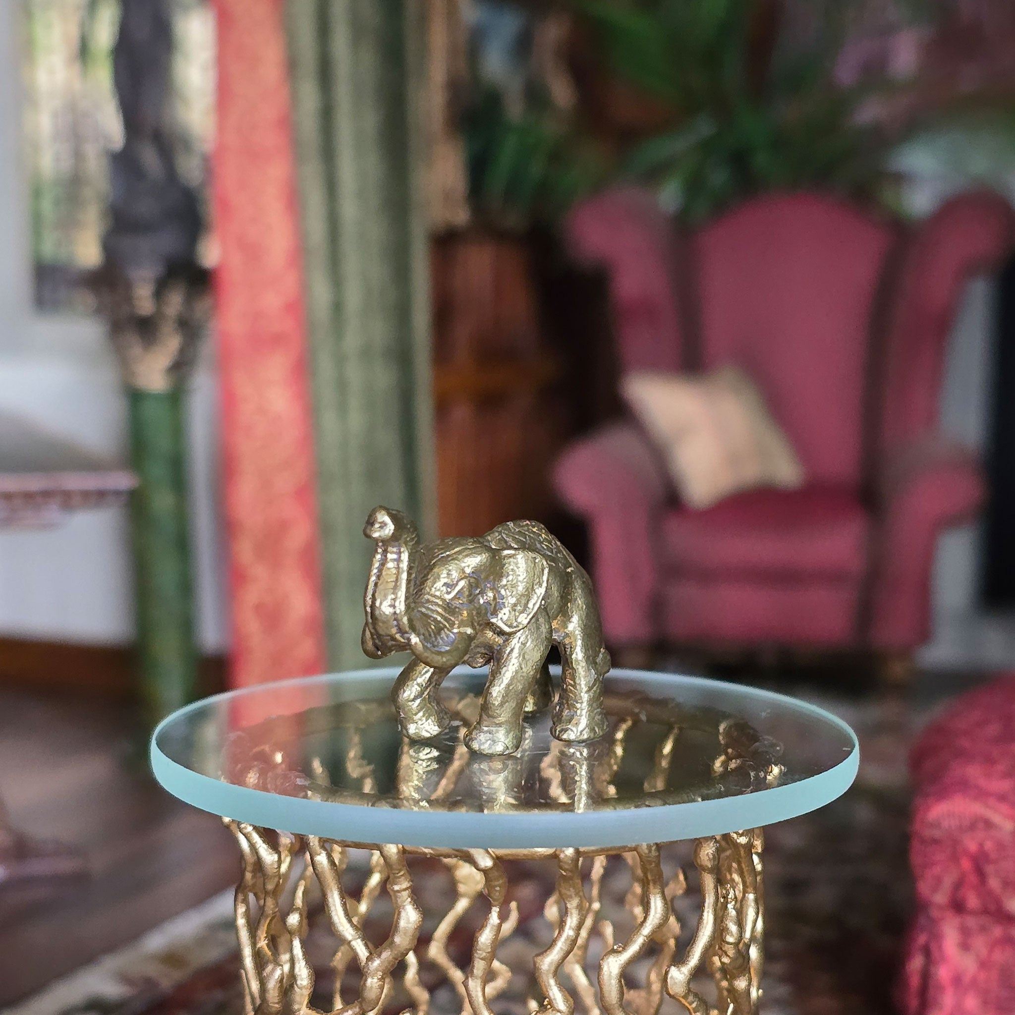 Gold elephant figurine on a glass table with a blurred background of a living room.