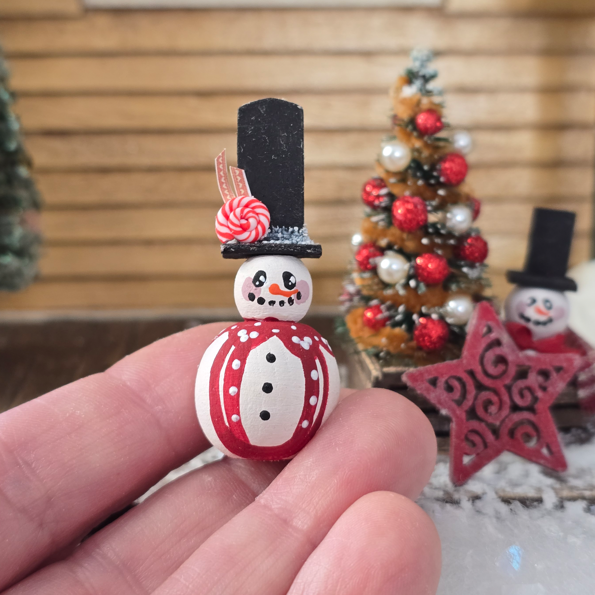 Small decorative snowman figure held in a hand with a Christmas tree in the background